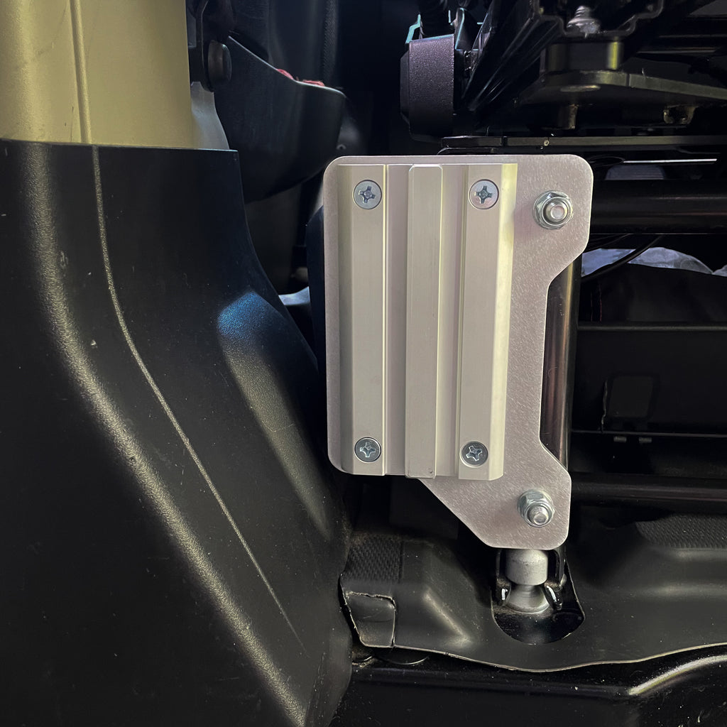 Ram ProMaster Lagun table mount wide bracket installed on driver side factory seat base, CNC machined aluminum no-drill mount showing full bracket face and M10 bolt attachment
