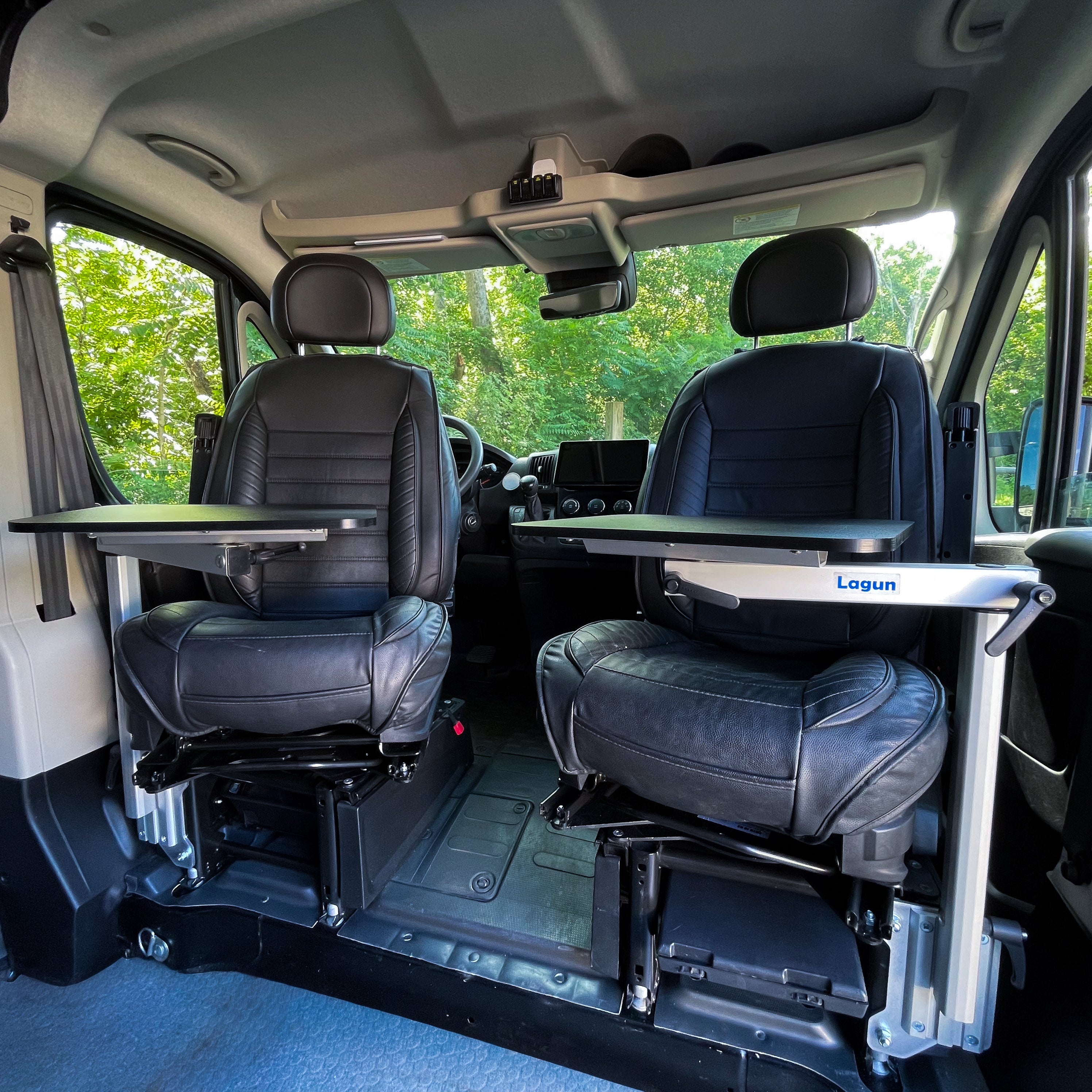 ProMaster Lagun table mount installed on Ram ProMaster passenger seat base, both captain's chairs swiveled with tables deployed, sliding door open
